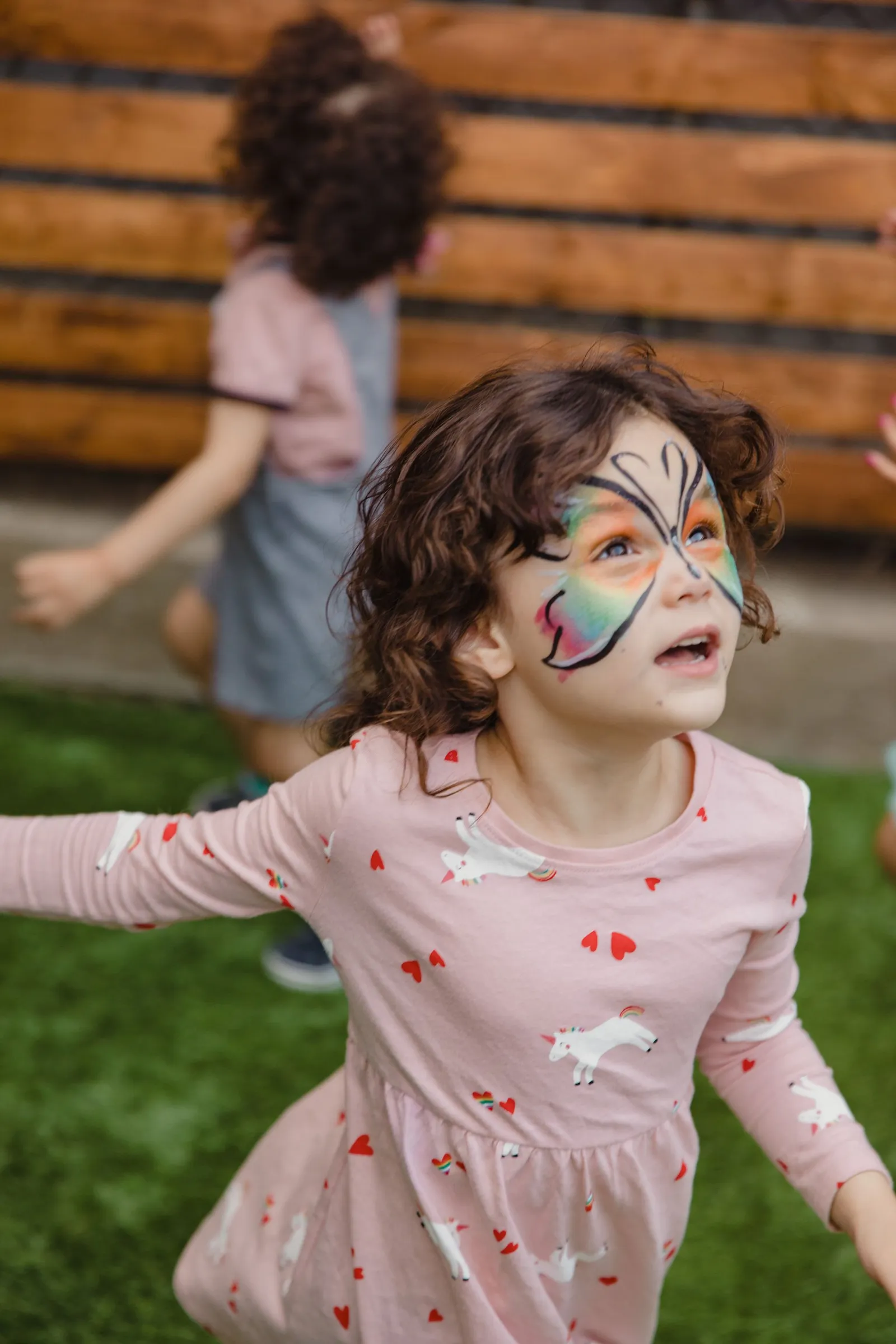 Child with butterfly face paint running across a lawn at a party