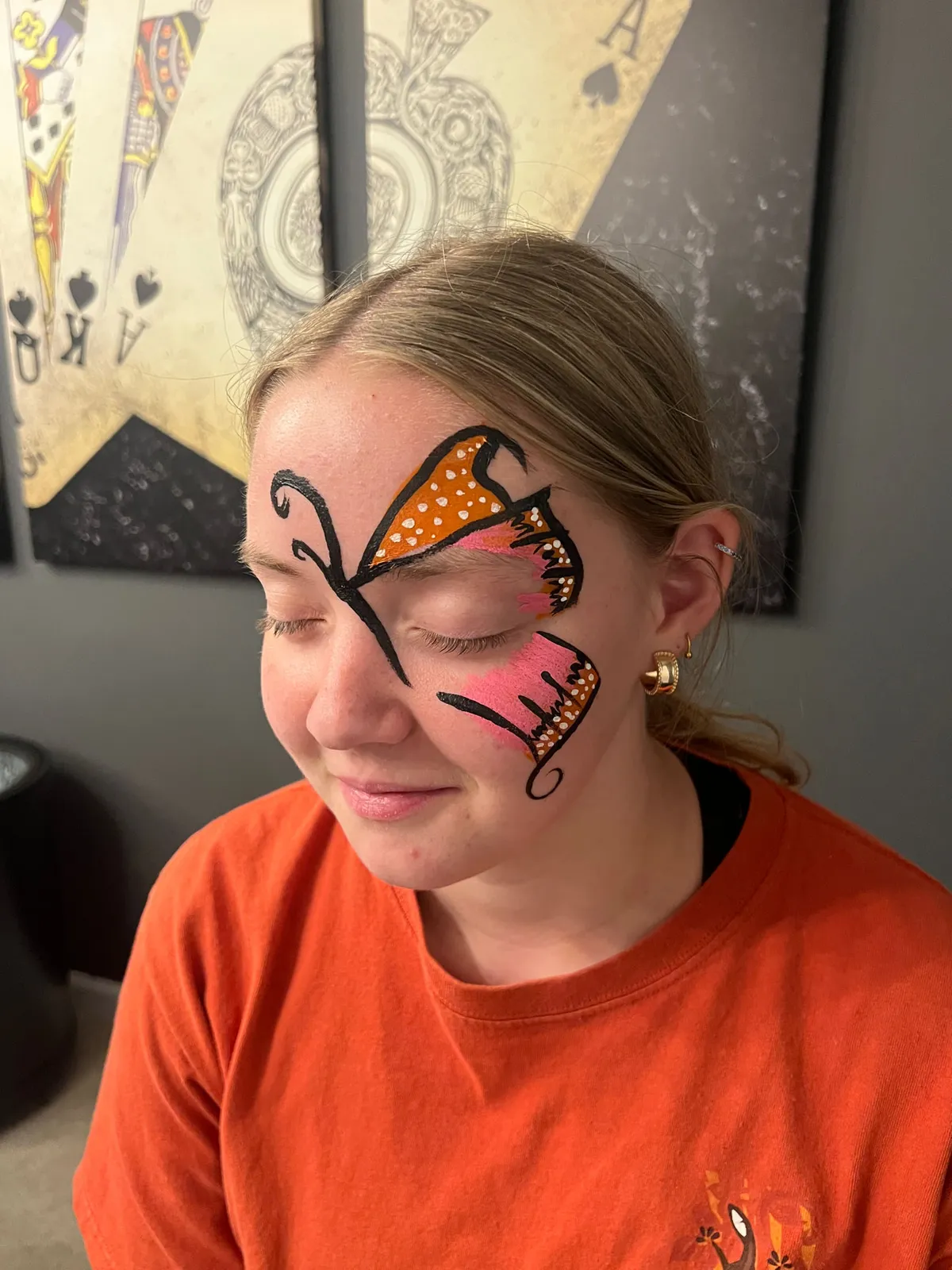 Orange and pink butterfly wings with white dots, painted across the forehead and brow
